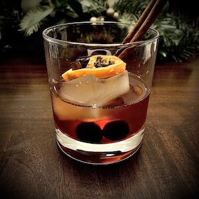 A Holiday Spiced Orange Old Fashioned cocktail in a rocks glass, garnished with a cinnamon stick and dehydrated orange slice.